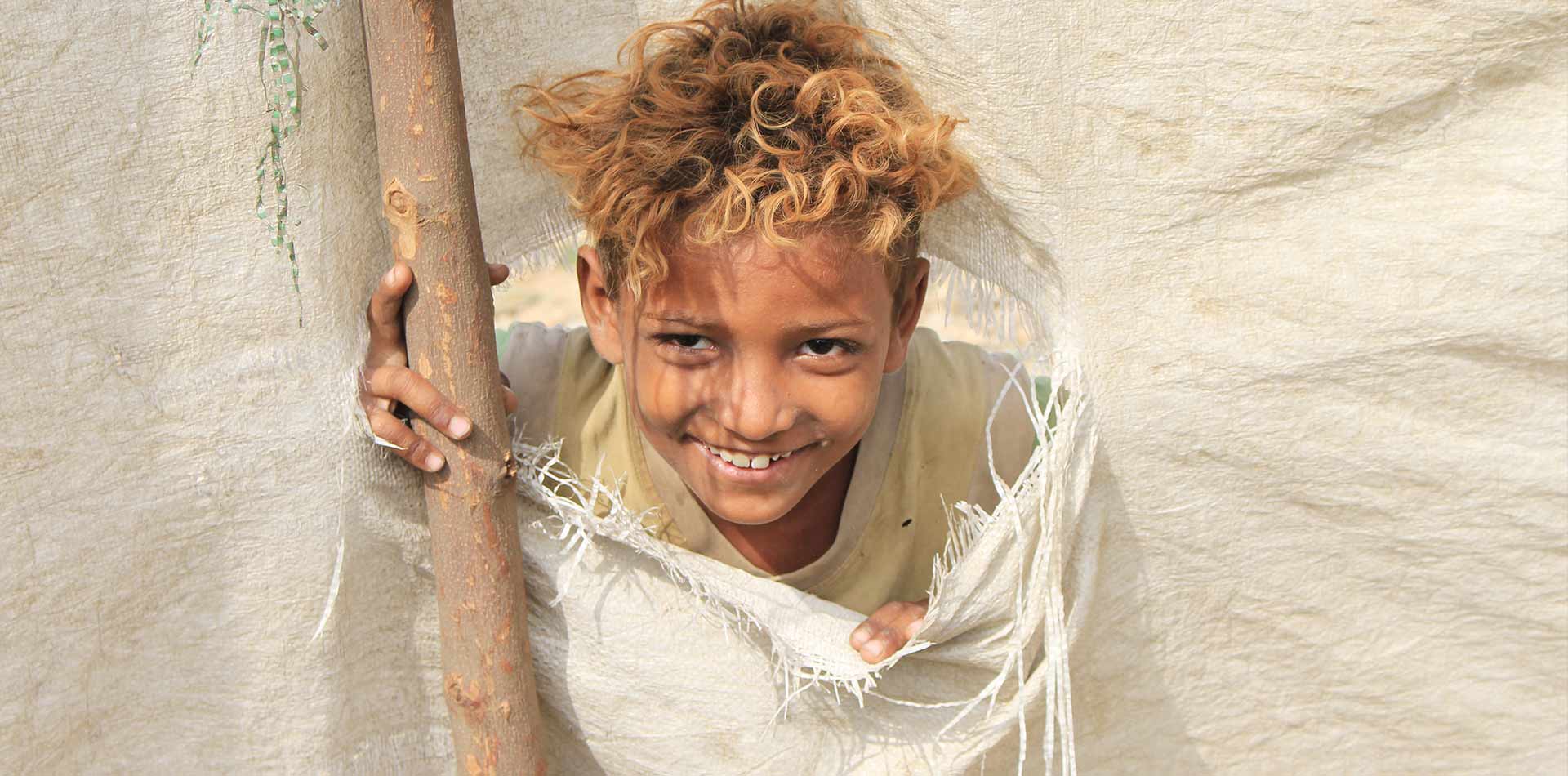 طفل يمني نازح يبتسم من خيمة ممزقة
